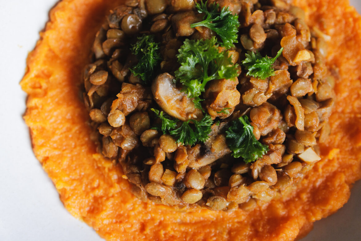 Veganské ragú z čočky a hub, servírované na lůžku batátové kaše, sypané petrželkou