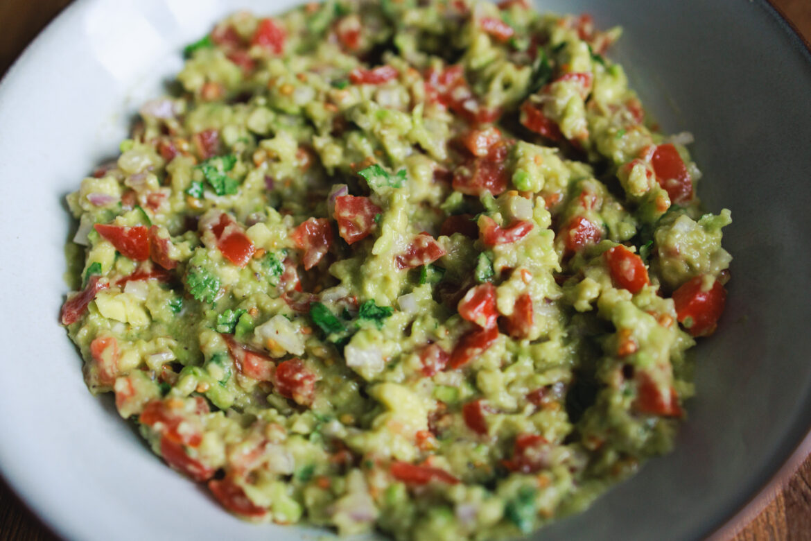 Recept na guacamole: Avokádo rozmačkané s nakrájenými rajčaty, koriandrem a šalotkou, zakápnuté limetkou a zamíchané v hlubokém talíři
