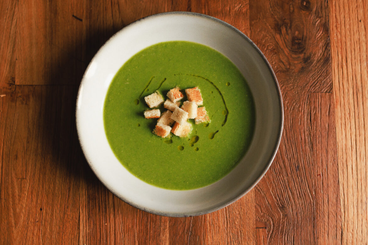 Veganská zelená krémová polévka z hrášku, edamame a špenátu, zdobená pečenými krutony a zakápnutá olivovým olejem